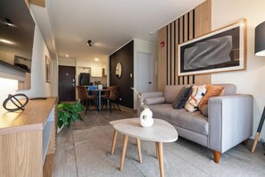 A modern living room with a grey sofa, a coffee table, and a dining area in the background. - Stylish Gálvez 370 Apartments By Geko (Miraflores)