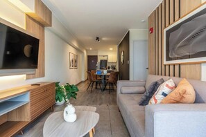 A modern living room with a flat-screen TV, a sofa, a dining area, and a kitchen in the background. - Stylish Gálvez 370 Apartments By Geko (Miraflores)