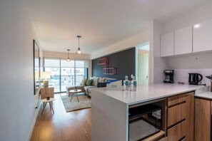 A modern kitchen with white cabinets, a central island, and a dining area with a sofa and table. - Suárez Signature Apartment By Geko (San Isidro)