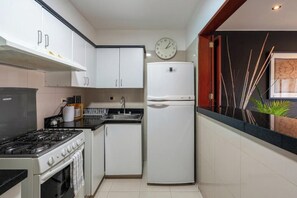 Eine kleine Küche mit weißen Schränken, einem Herd, einer Spüle und einem Kühlschrank.