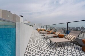 Eine Dachterrasse mit Pool, Liegestühlen und einem gemusterten Boden.