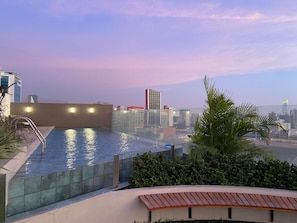 An outdoor swimming pool with a cityscape view, surrounded by greenery and modern buildings. - Plaza 27 Residences By Geko (Miraflores)