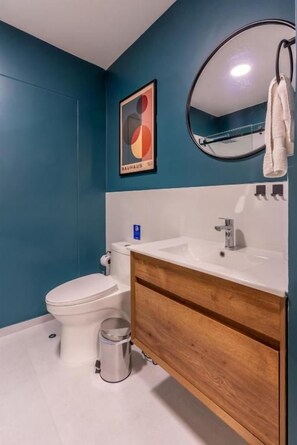 A bathroom with a toilet, sink, mirror, and a Bauhaus poster on the wall. - Juan Norberto Eléspuru 535 Apartments By Geko (San Isidro)