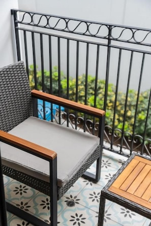 A balcony with a wicker chair and a small table, featuring a metal railing and patterned floor tiles. - Charming Barranco Apartments By Geko (Barranco)