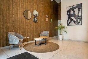 A lobby with a wooden wall, two armchairs, a small table, a potted plant, and abstract art. - Modern Benavides 707 Residences By Geko (Miraflores)