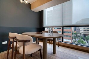 A modern room with a round table, four chairs, a large window with a city view, and a ceiling light fixture. - Modern Benavides 707 Residences By Geko (Miraflores)