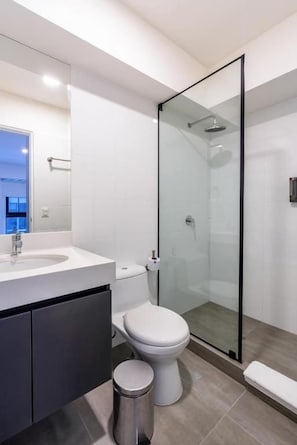 A modern bathroom with a glass shower enclosure, a white toilet, and a sink with a dark cabinet. - Modern Benavides 707 Residences By Geko (Miraflores)