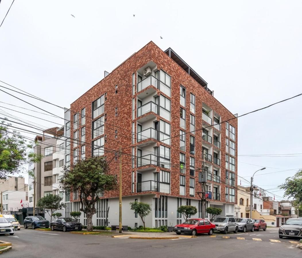 Un edificio de varios pisos con fachada de ladrillo, balcones y un estacionamiento con automóviles.