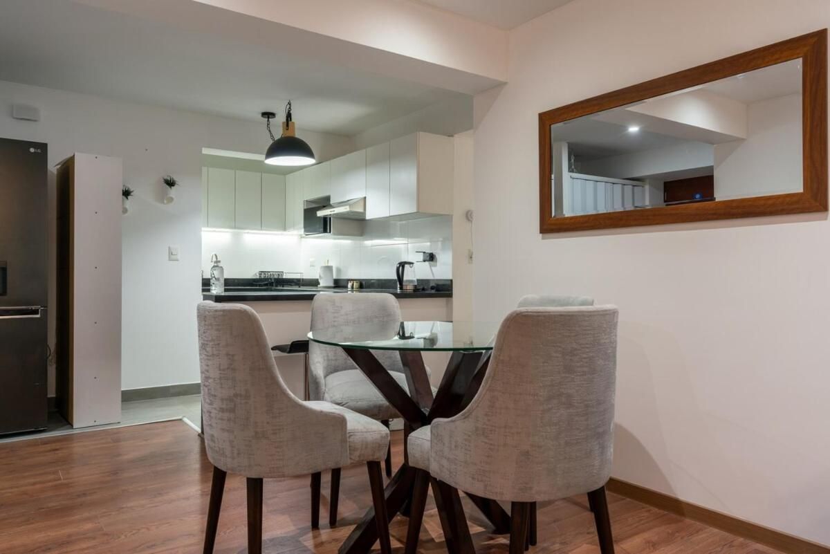 Una cocina moderna con armarios blancos, un refrigerador negro y una mesa de vidrio con cuatro sillas.