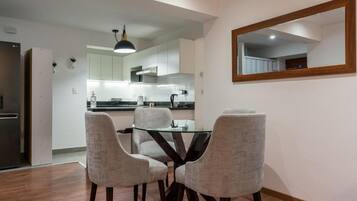 Una cocina moderna con armarios blancos, un refrigerador negro y una mesa de vidrio con cuatro sillas.