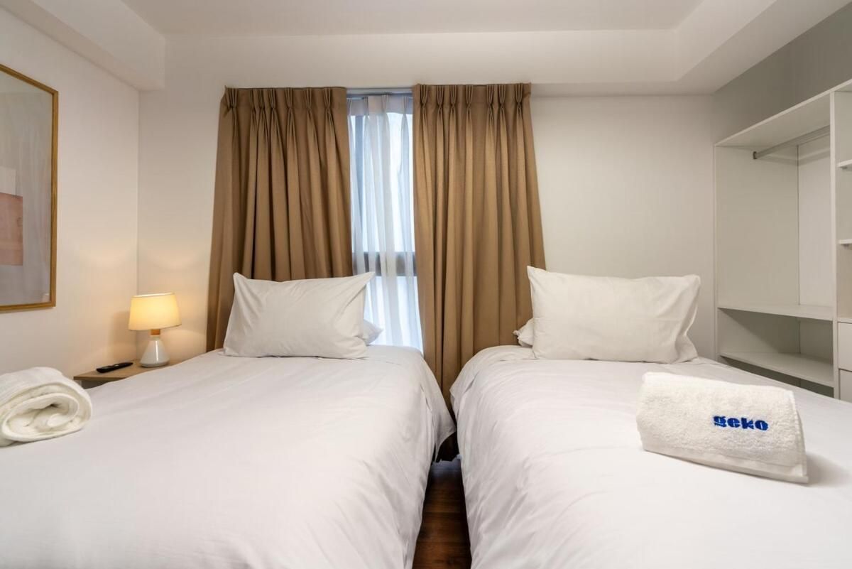 Habitación de hotel con dos camas, una mesita de noche con lámpara, una toalla y un espejo.