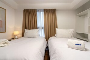 A hotel room with two beds, a nightstand with a lamp, a towel, and a mirror. - Elegant Los Angeles Apartments By Geko (San Isidro)