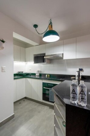 Cozinha moderna com armários brancos, bancada verde e luminária pendente.