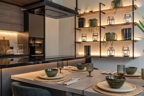 A modern kitchen with a dining area, featuring a marble countertop, a built-in oven, and a wall-mounted shelf with decorative items. - Magdalena Style Suites & Apartments (Magdalena del Mar)
