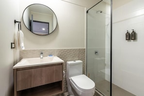 A modern bathroom with a glass-enclosed shower, a round mirror, and a white toilet. - Magdalena Style Suites & Apartments (Magdalena del Mar)