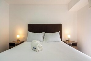 A hotel room with a large bed, two bedside tables with lamps, and a rolled towel on the bed. - San Isidro Petit Thouars Living By Geko (San Isidro)