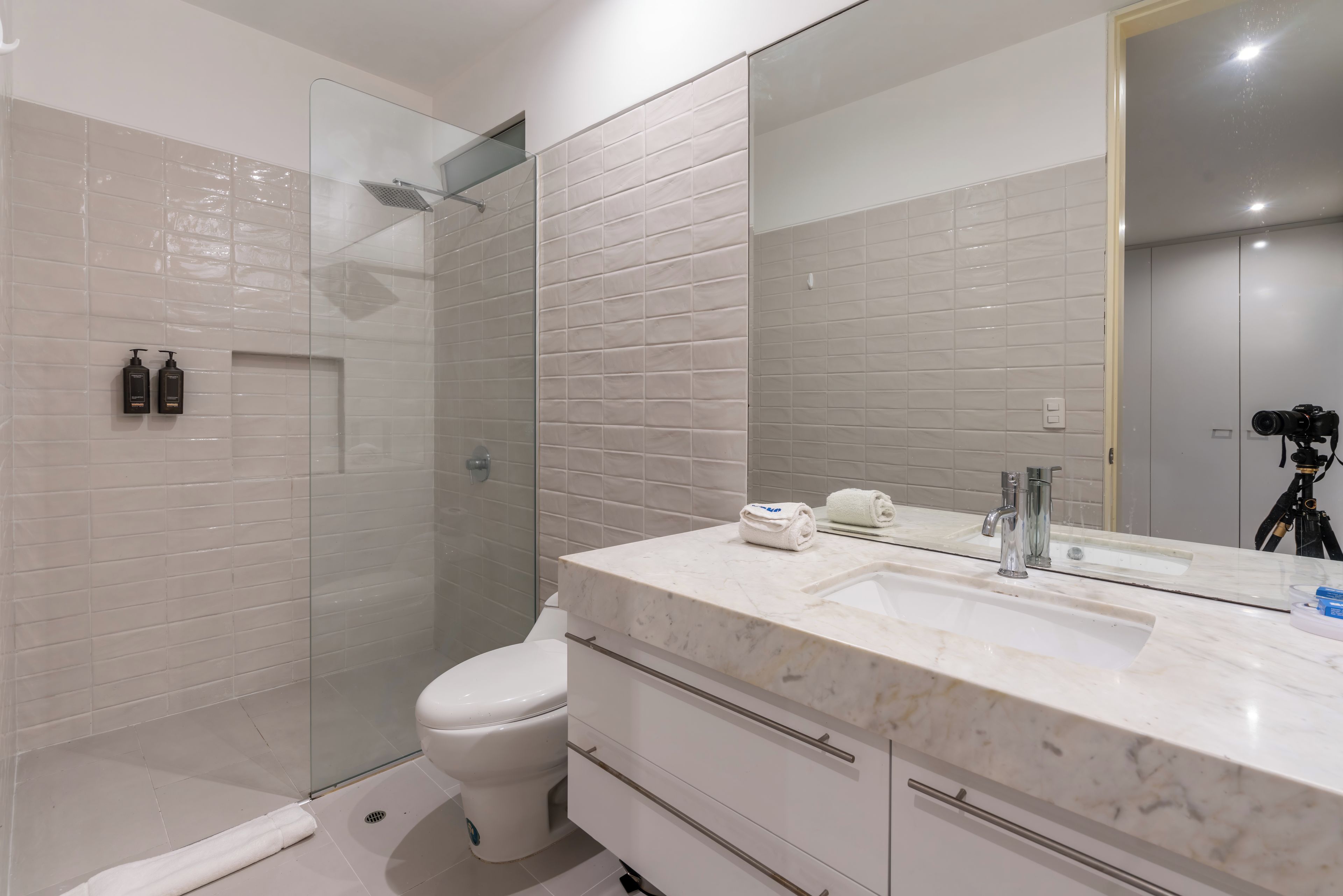 A modern bathroom with a glass shower enclosure, a white toilet, a marble sink, and a large mirror.