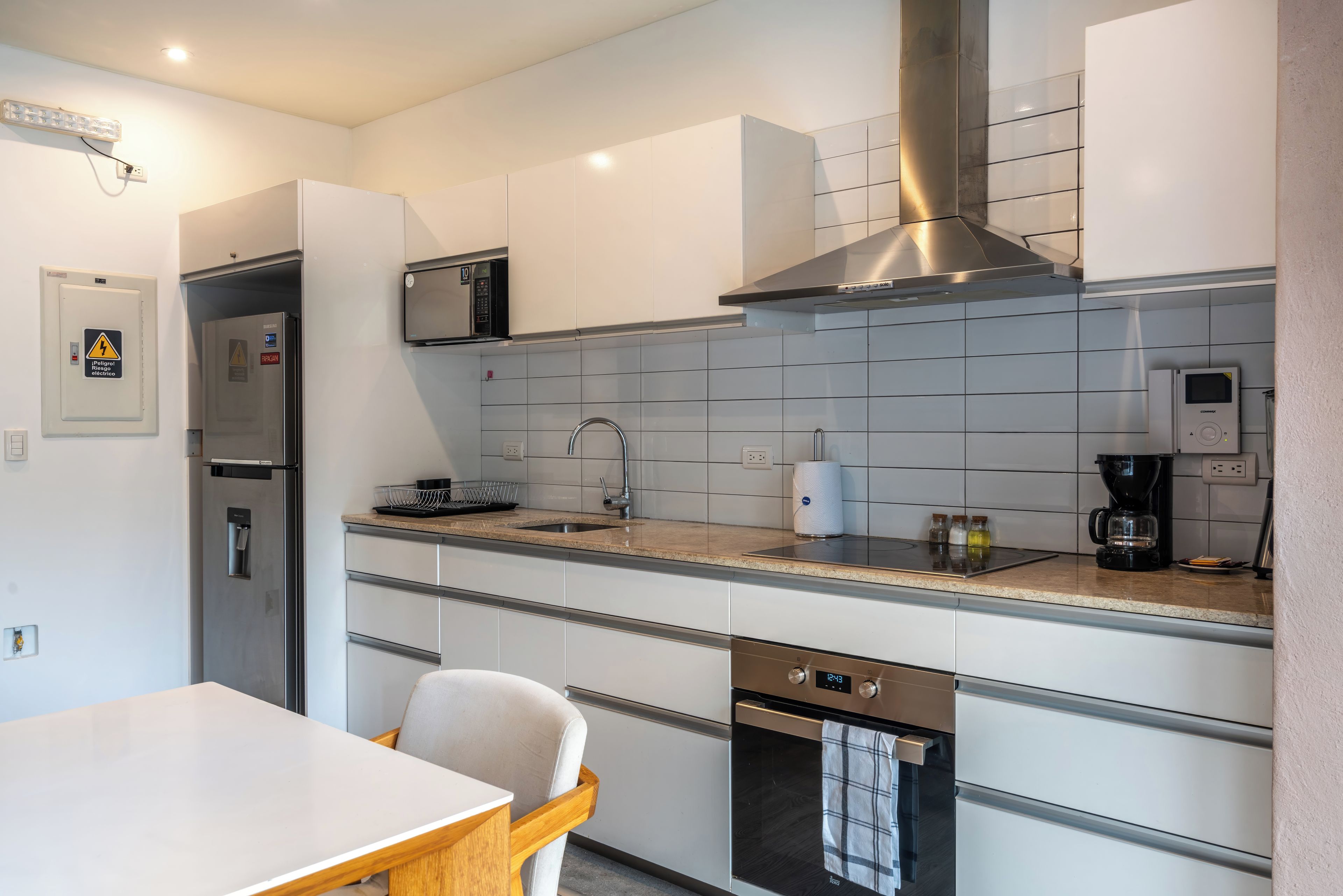 Una cocina moderna con armarios blancos, una campana extractora de acero inoxidable, microondas y cafetera.