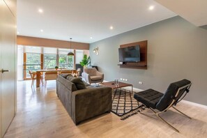 Ein modernes Wohnzimmer mit einer Couch, einem schwarzen Sessel, einem Couchtisch und einem an der Wand montierten Fernseher.