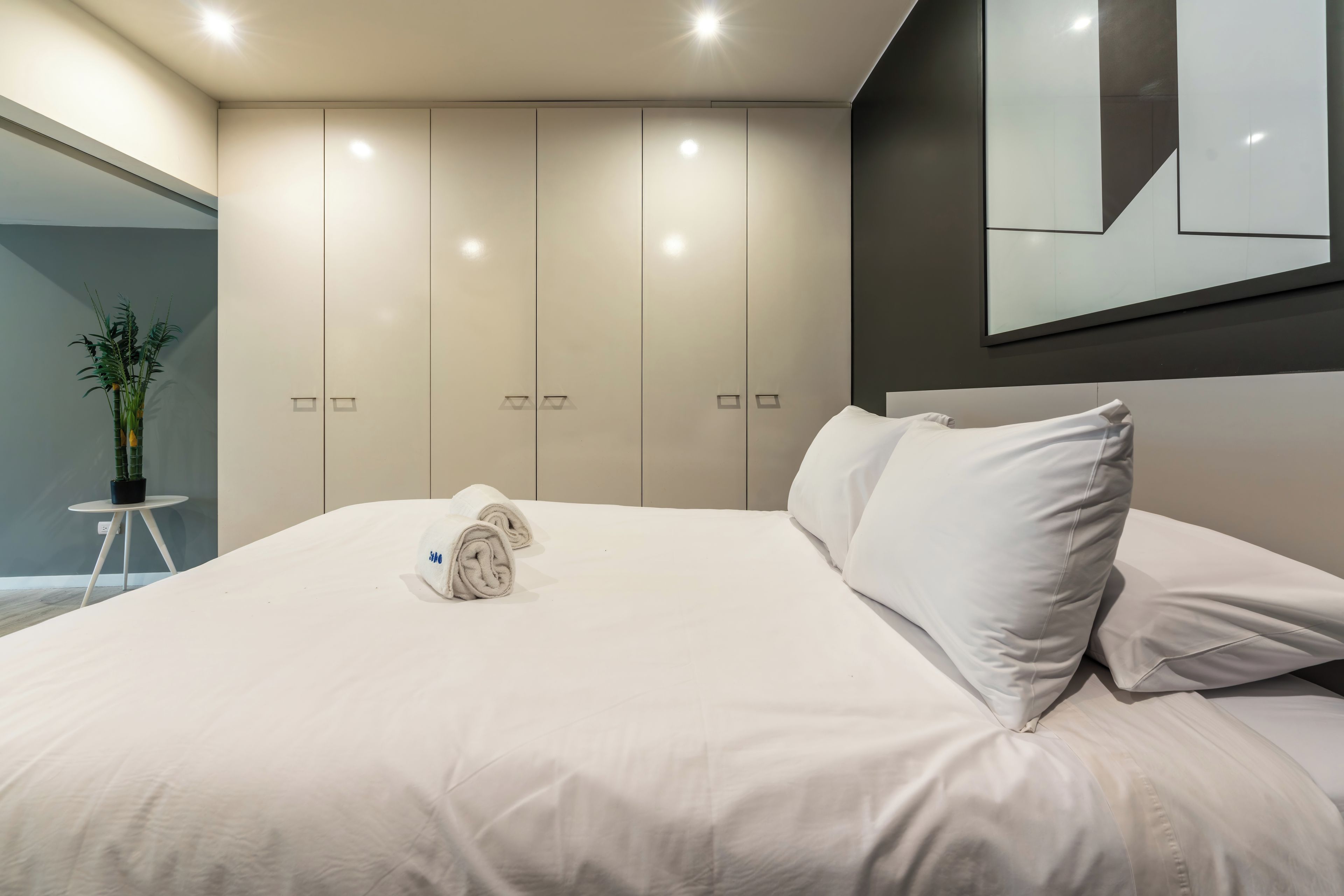 A modern bedroom with a large bed, a small round table, and a potted plant.