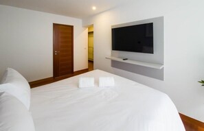 Una habitación de hotel con una cama, un televisor montado en la pared y una puerta que da a otra habitación.