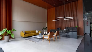 A modern lobby with a yellow sofa, wooden chairs, a coffee table, and a reception desk. - Javier Prado Executive Apartments By Geko (Lima)