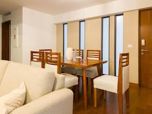 A dining area with a wooden table and chairs, a sofa, and a sliding door with frosted glass panels. - Javier Prado Executive Apartments By Geko (Lima)