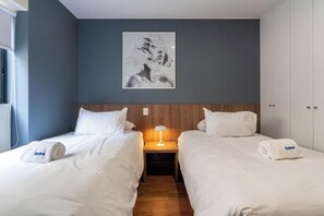 A hotel room with two beds, a nightstand with a lamp, a wooden headboard, and a framed artwork on the wall. - Miraflores Canseco Apartments By Geko (Lima)