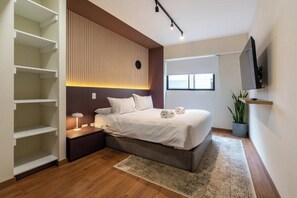 A modern bedroom with a bed, bedside tables, a TV, and a window. - Miraflores Canseco Apartments By Geko (Lima)