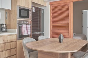 A modern kitchen with a microwave, oven, and coffee maker, a wooden dining table with chairs, and a sliding wooden door. - Vasco Núñez Residence By Geko (Miraflores)