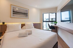 A modern hotel room with a large bed, a desk, and a view of the city through a large window. - Vasco Núñez Residence By Geko (Miraflores)