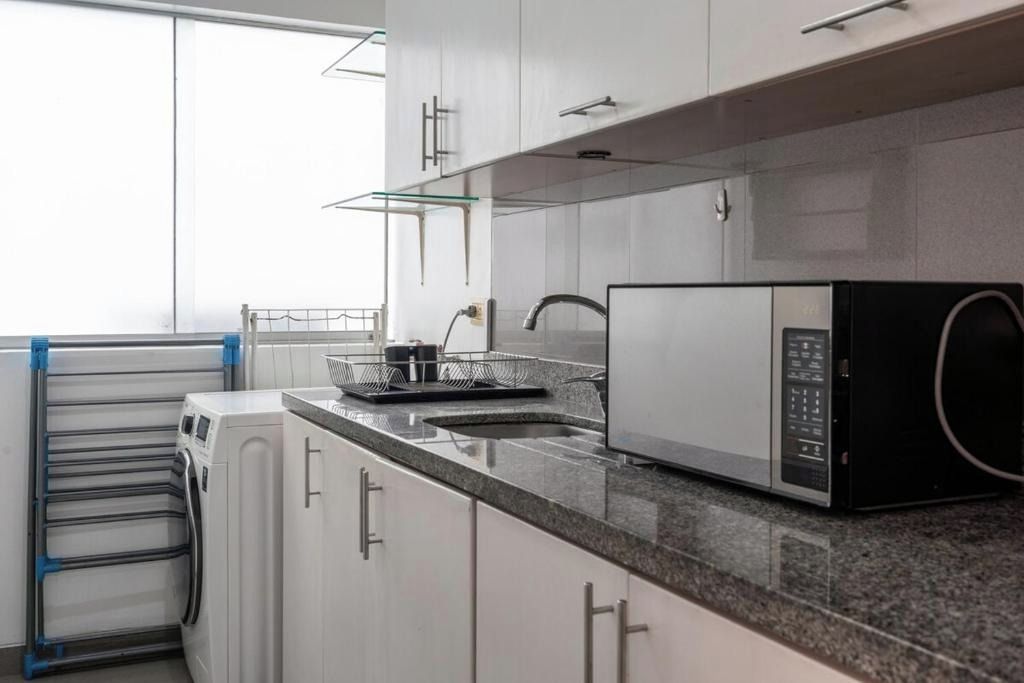 A kitchen with white cabinets, a stainless steel sink, a microwave, and a drying rack.