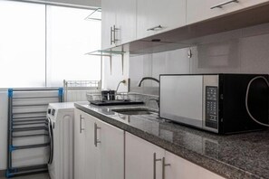 Una cocina con armarios blancos, un lavamanos de acero inoxidable, un microondas y un tendedero.