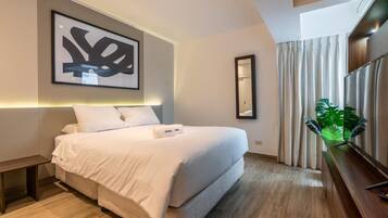 A hotel room with a large bed, a bedside table, a TV, and a plant.