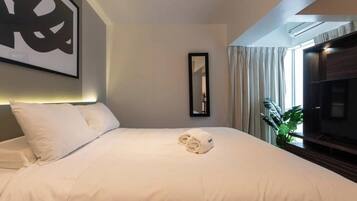 A hotel room with a bed, a mirror, a television, and a plant.