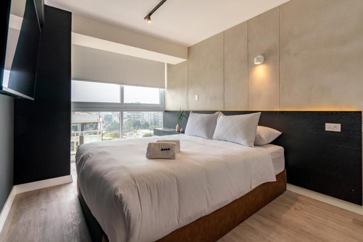 A modern hotel room with a large bed, a flat-screen TV, and a city view.