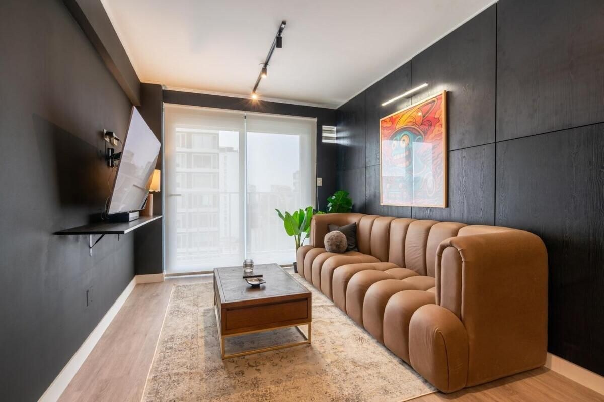 A modern living room with a brown leather sofa, a coffee table, and a large window.