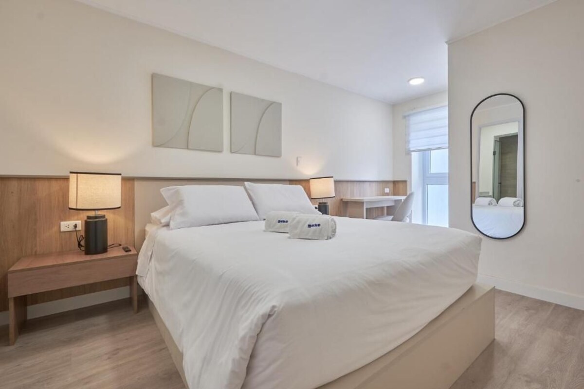 A hotel room with a bed, bedside lamps, a nightstand, a mirror, and artwork on the wall.
