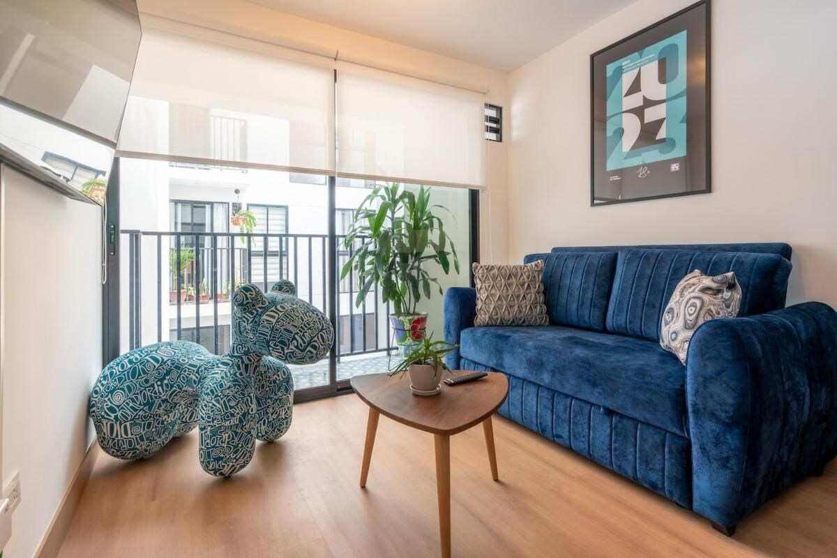 A modern living room with a blue sofa, a round wooden coffee table, and a large window with a view of the outside.