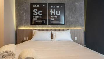 Camera d'albergo con un letto grande, due cuscini, un asciugamano piegato con cura e un display a parete con parole e numeri motivazionali.