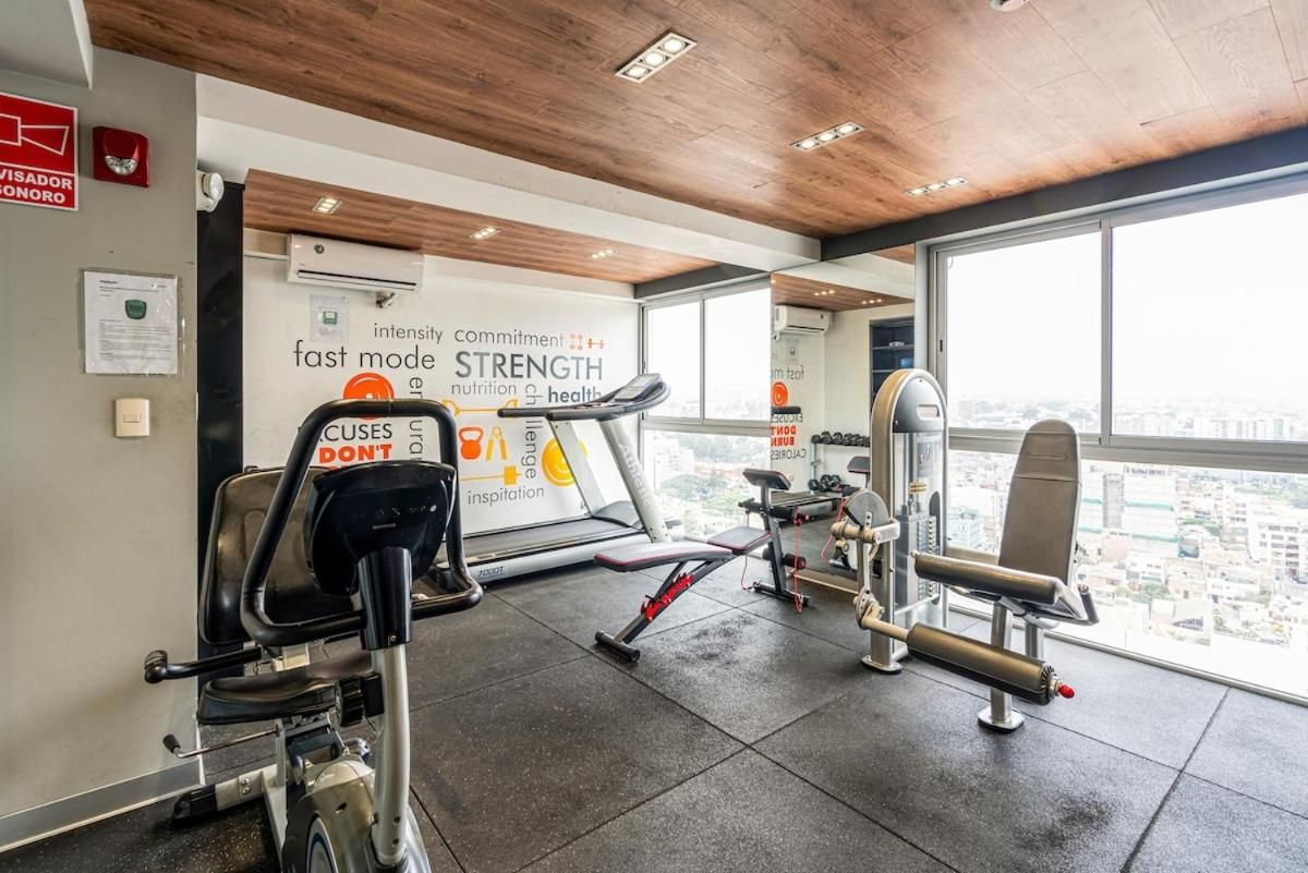 A gym with exercise equipment, a motivational poster, and a view of the city through large windows.