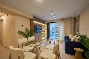 A modern living room with a glass dining table, white chairs, a blue sofa, and a large window with curtains. - Larco 791 Luxury Stays By Geko (Miraflores)