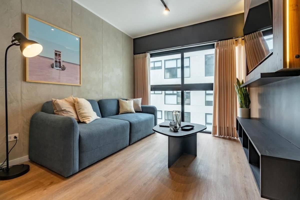 Ein modernes Wohnzimmer mit einer Couch, einem Couchtisch, einer Stehlampe und einem großen Fenster mit Vorhängen.
