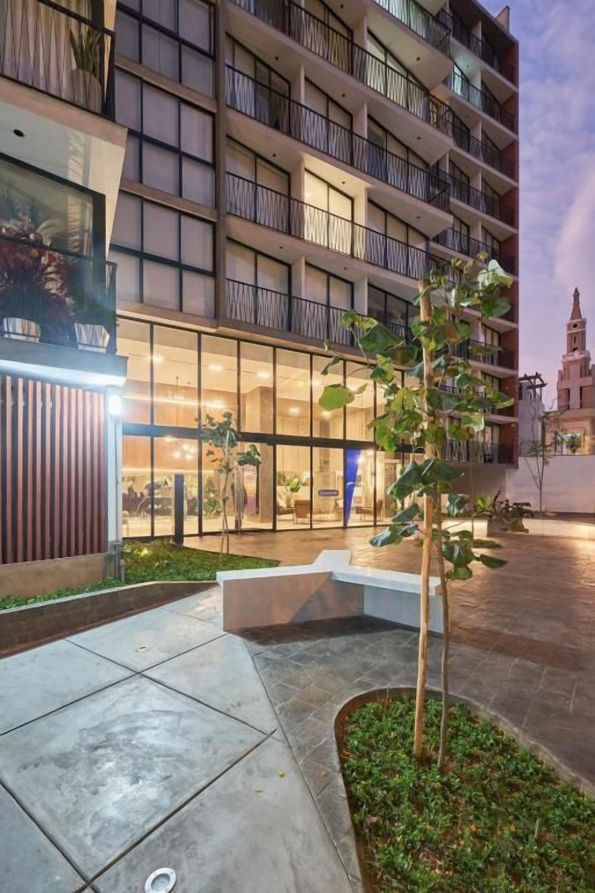 Ein mehrstöckiges Hotel mit Balkonen, einem gut beleuchteten Eingangsbereich und einem angelegten Innenhof.