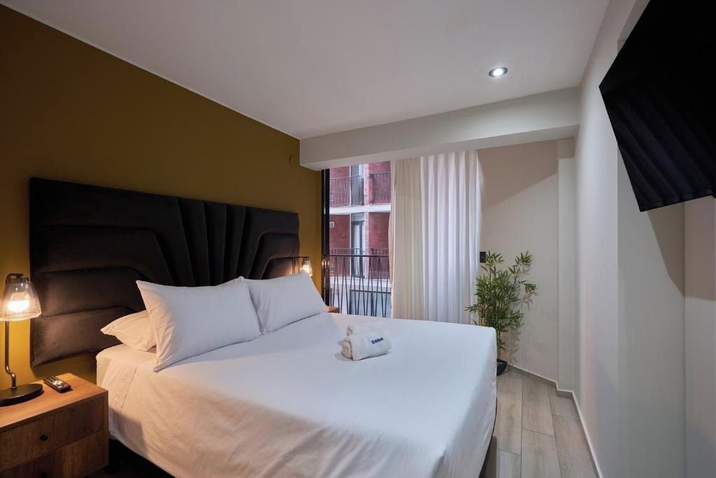 Ein Hotelzimmer mit Bett, Nachttisch mit Lampe, einem Fenster mit Vorhängen und Blick auf ein Gebäude.