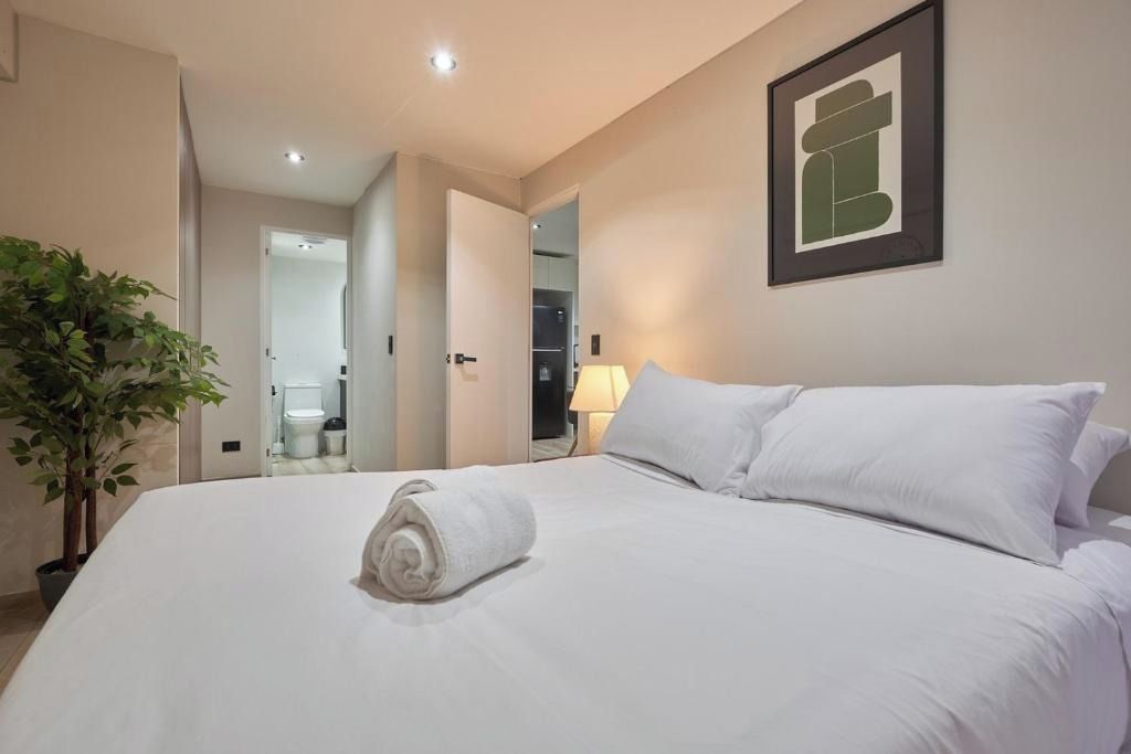 A hotel room with a neatly made bed, a potted plant, and a framed picture on the wall.