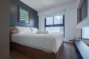 A modern bedroom with a wooden bed, a large window, and a wall-mounted artwork. - Miraflores Intimate Apartment By Geko (Miraflores)