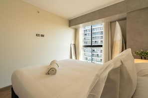 Una habitación de hotel con una cama, una ventana con cortinas, una tabla de surf y una pequeña mesa con una planta.