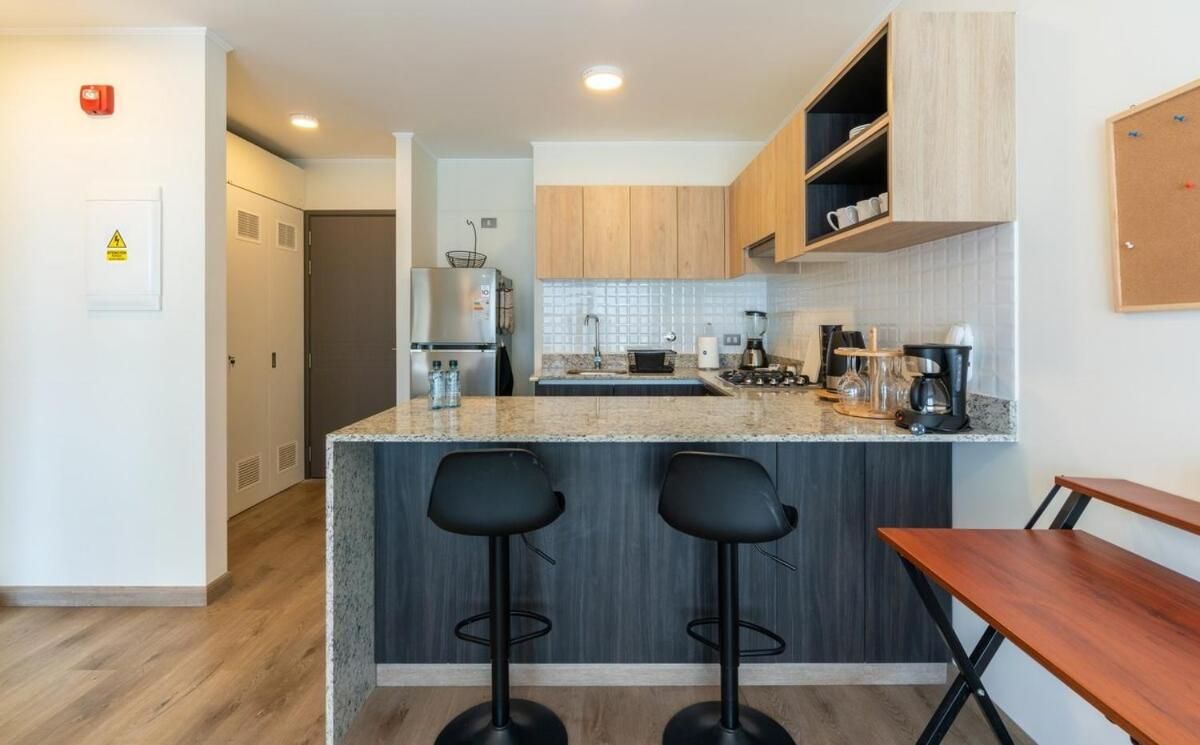 Una cocina moderna con encimera de granito, dos taburetes de bar, una mesa de comedor de madera y un horno empotrado.