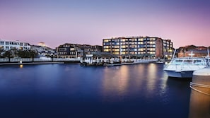 Hotel na orla com vários andares, um cais com barcos e um rio calmo.